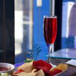 A glass of red drink on a table next to a plate of colorful tortilla chips with dips in small bowls.