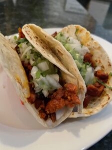 Two tacos on a white plate, each filled with chopped seasoned meat, diced onions, and cilantro.