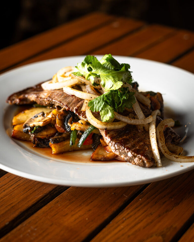 A plate of cooked steak topped with onions and cilantro, served over mixed vegetables on a wooden table.