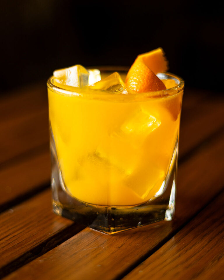 A glass of orange juice with ice cubes and orange slices on a wooden table.