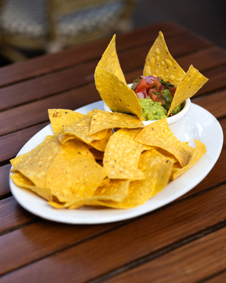 A plate of tortilla chips with a small bowl of guacamole and salsa on a wooden table.